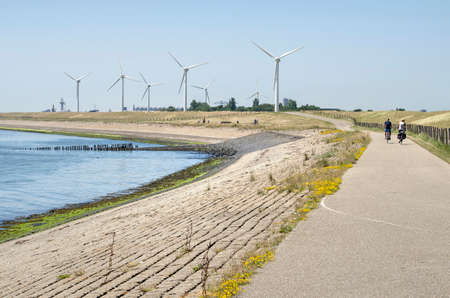 Vlissingen, The Netherlands, June 29, 2019: bicycle path along the coast of Westerschelde estuary with a group of wind turbines in the backgroundのeditorial素材