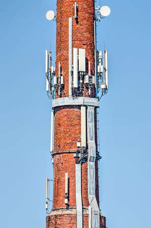 Old red brick chimney, largely covered with antennas and other modern technology against a blue skyのeditorial素材