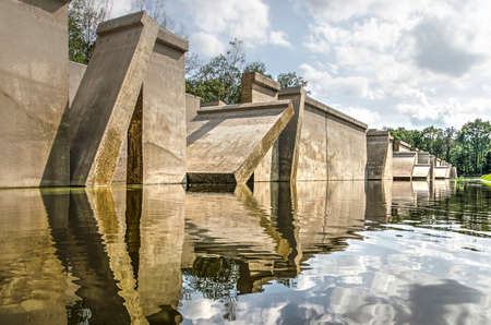 Kraggenburg, The Netherlands, August 4, 2019: low angle view of the concrete "Deltagutter", former experimental hydraulic facility, reflecting in th surrounding pond, in Waterloopbos national monumentのeditorial素材