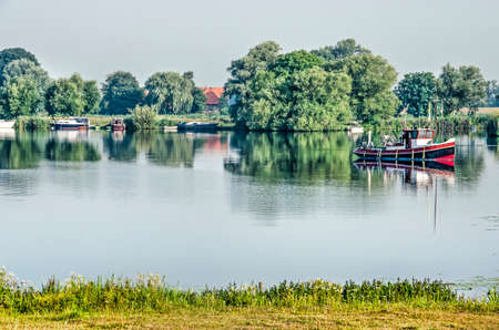 Tranquil scene at the banks of Zwarte Water (Black Water) river near Zwolle, The Netherlands, with boats and trees reflecting under a blue sky on a summer morningの写真素材