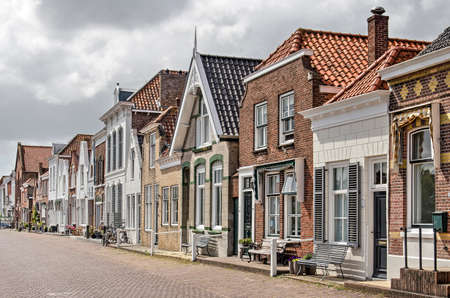 Brouwershaven, The Netherlands, August 10, 2019: row of old one or two storey brick and plastered houses facing the town's harbourのeditorial素材