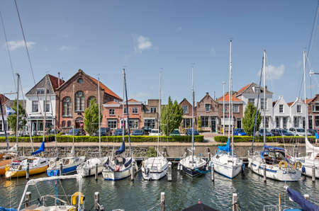 Brouwershaven, The Netherlands, August 10, 2019: the town's harbour with yachts moored and on the other quay a row of historic houses under a blue sky on a summer dayのeditorial素材