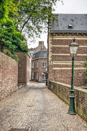 Maastricht, The Netherlands, September 8, 2019: view along a narrow street in the old town with brick walls and houses, a lantern and a treeのeditorial素材