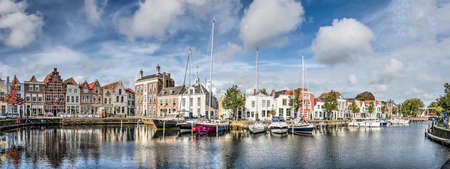 Goes, The Netherlands, October 9, 2019: panoramic composite view of the entire western and northern side of the old harbour with historic houses, modern yachts and reflective waterのeditorial素材