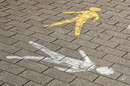 Two pedestrian symbols painted in different colors and directions on a brick pavementのeditorial素材