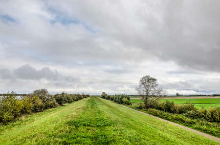 Hiking path on a grass dike along lake Grevelingen under a cloudy sky on the island of...