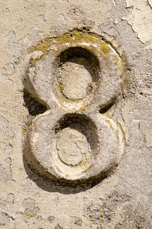 The number 8 embossed on a weathered stony surface, partly covered with lichen and peeling plasterのeditorial素材