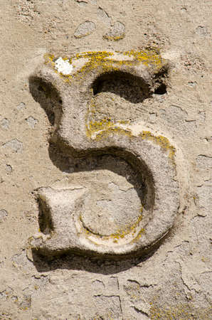 The number 8 embossed on a weathered stony surface, partly covered with lichen and peeling plaster