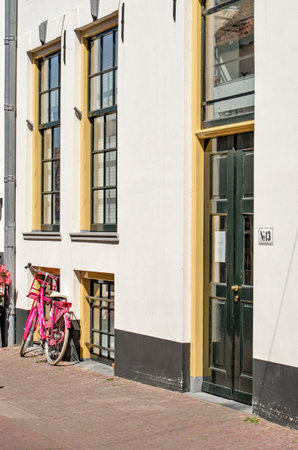 Hattem, The Netherlands, July 31, 2020: Facade in the old town with white plaster and green and yellow window frames and a pink bicycleのeditorial素材