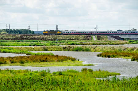 Kampen, The Netherlands, July 26, 2020: view across the wetlands around the new Reevediep river channel with in the background a bridge with a train bound for Germanyの写真素材