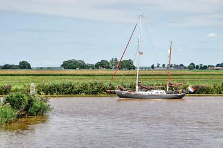 Kamperzeedijk, The Netherlands, August 2, 2020: sailing yacht navigating by motor in a canal in a characteristic frlat green Dutch polder landscapeのeditorial素材