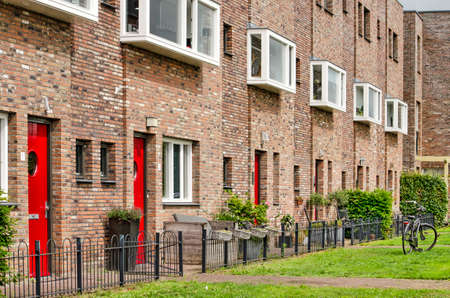 Oud-Beijerland, The Netherlands, July 10, 2020: row of recently built townhouses with red doors, brick facade, baywindows and a green lawnのeditorial素材