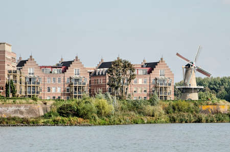 Gorinchem, the Netherlands, September 23, 2020: view from the river Merwede towards the city walls with a recenly built housing complex in traditional style and a historic windmillのeditorial素材