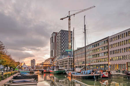 Rotterdam, The Netherlands, November 5, 2020: Dramatic sky at susnet over Wijnhaven harbor with sloops, historic barges, modern architecture and a construction craneのeditorial素材