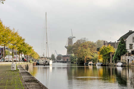 Schiedam, the Netherlands, October 23, 2020: a mix of modern and traditional industries around Buitenhaven (outer harbor) with a sailboat and the Nolet windmillのeditorial素材