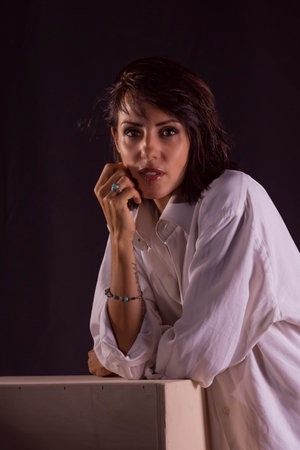 portrait of young woman with black hair dressed in a white shirt thoughtfully looking at the camera on black background woman portraitsの写真素材