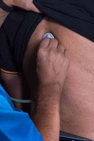 mature doctor with a beard dressed in a blue operating room suit on a black background examining a patient health medical professionsの写真素材