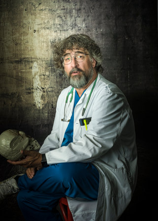 doctor with a beard dressed in a blue operating room suit and white coat holds a caravel in his handの写真素材