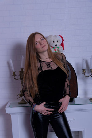 young woman with a piercing and long hair rests by a white fireplace and has an antique radio on top of which is a teddy bear with a red christmas hat and white candle holdersの写真素材