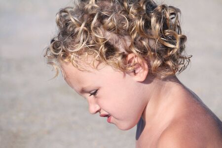 a young child looking down sitting in the sun by the beachの写真素材