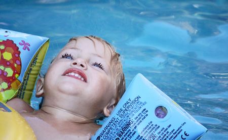 a toddler floating in a swimming pool looking upの写真素材