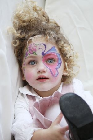portrait of a young child with her face painted and foot in the air looking towards the cameraの写真素材