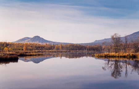 A pure reflection of the mountains and autumn forest in the calm surface of the lakeの写真素材