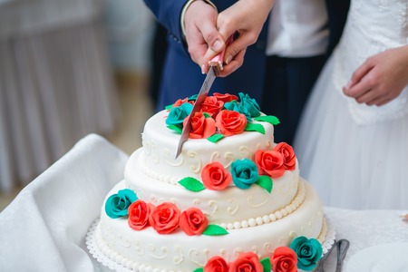 Newlyweds cutting delicious wedding cake with colorful flowersの写真素材