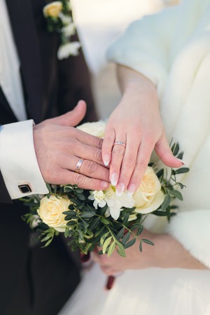 Hands of newlyweds with rings on wedding bouquetの写真素材