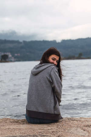 Woman is seeing and relaxing while she is sitting in fornt of the sea. She is looking at the camera.の写真素材