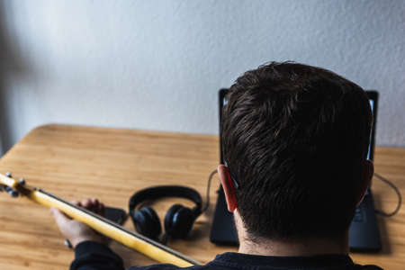 Man is learning how to play the guitar with his earphones and the laptopの写真素材