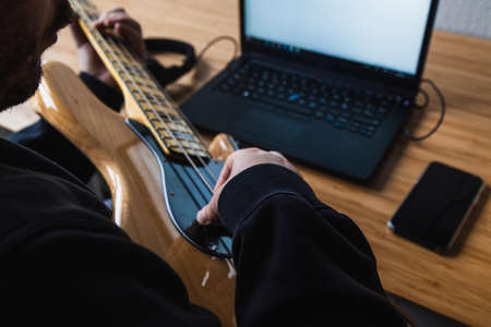 Man is learning how to play the guitar with his earphones and the laptopの写真素材
