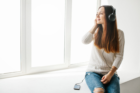 Beautiful girl is listening to the music next to the windowの写真素材