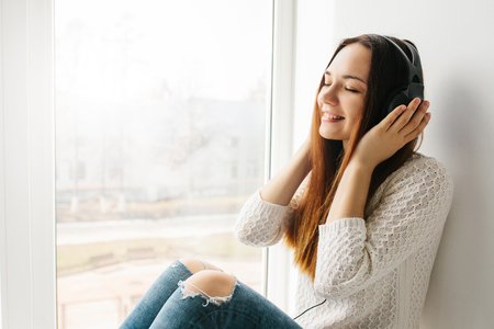 Beautiful girl is listening to the music next to the windowの写真素材