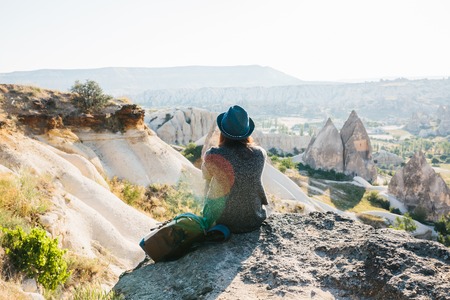 A traveler in a hat with a backpack stands on a mountain and looks at a beautiful view in Cappadocia in Turkey. Journey. Hiking.の写真素材