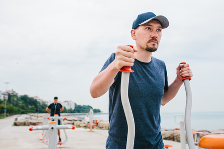 A man trains on sporting equipment in a city in the open air. The concept of a healthy lifestyle and accessibility of sports training for every person. Available sports equipment in a public place.の写真素材