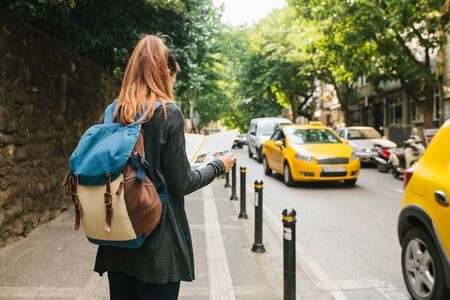 A young tourist girl with a backpack in a big city is watching a map. Journey. Sightseeing. Travel.の写真素材