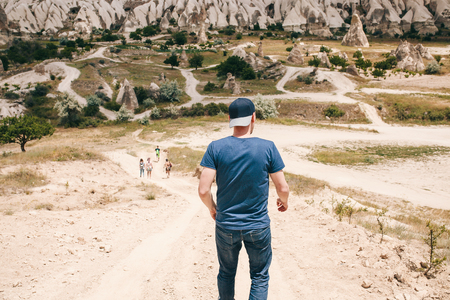 The tourist guy is trying to catch up with his friends of tourists on the road in the hilly countryside of Cappadocia in Turkey. Hiking, travel, walk, rest.の写真素材