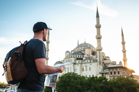 A traveler in a baseball cap with a backpack is looking at the map next to the blue mosque - the famous sight of Istanbul. Travel, tourism, sightseeing.の写真素材