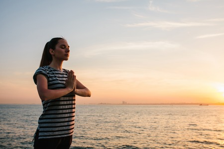 Young beautiful girl practicing yoga and meditation on the rocks next to the sea at sunset. Sport. Yoga. Meditation. Recreation. Vacation. Relaxation.の写真素材