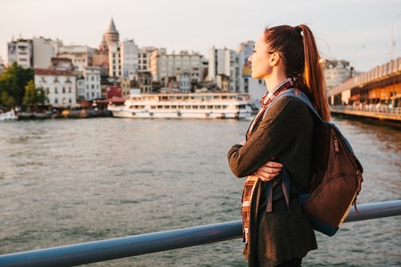 Young beautiful tourist girl with a backpack at sunset next to the Bosphorus on the background of Istanbul. Turkey. Rest, vacation, hiking.の写真素材