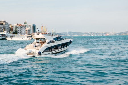 A speed boat sails along the blue water of the Bosphorus against the background of the European part of Istanbul. Scenic panoramic view. Travel, rest, vacation. Luxury holiday in Turkey.の写真素材