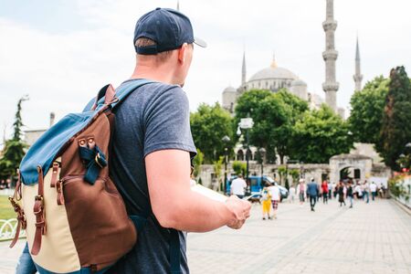 A traveler in a baseball cap with a backpack is looking at the map next to the blue mosque - the famous sight of Istanbul. Travel, tourism, sightseeing.の写真素材