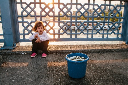Istanbul, June 15, 2017: Cute little girl sitting in front of a bucket of fish on the Galata bridge.のeditorial素材
