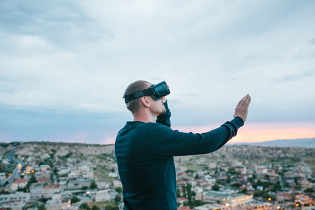 A man in virtual reality glasses on the background of a sunset over the city. Concept of future technologies. Modern technologies.の写真素材
