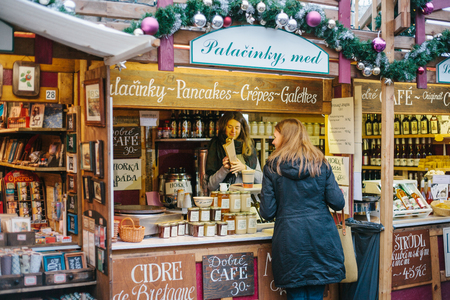 Prague, December 15, 2016: The seller offers the buyer a wide selection of honey and various wines. Christmas Market. The buyer is happy with the purchase. Celebrating Christmas in Europe.のeditorial素材
