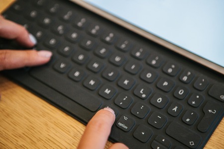 Hands on the tablet keyboard with German letters. The concept of remote work, freelancing, blogging,...