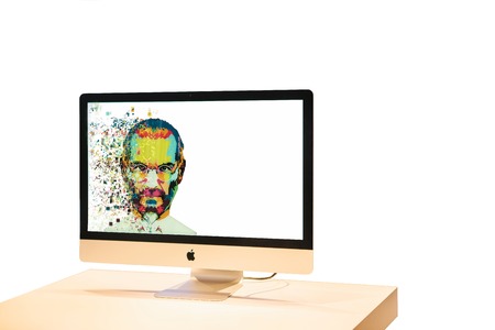 Computer Apple on a table on a white background with an illustration on the screen in an art style in the form of a mosaic of Steve Jobs fragmented with pixels.のeditorial素材