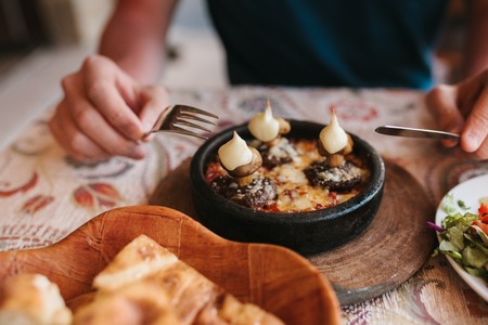 Mans hands holding cutlery - preparing to eat dish with mushrooms at table in cafeの写真素材