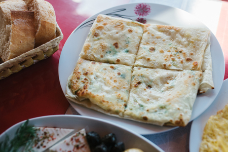 Flat cake with herbs divided into four pieces, piece of plate of vegetables and pieces of breadの写真素材